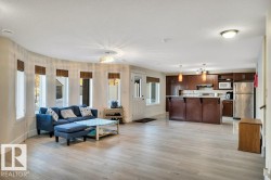 Open-concept living space featuring wood-finish flooring, a curved wall with multiple windows, recessed lighting, and a kitchen with wood cabinetry, stainless steel appliances, and a breakfast bar - 