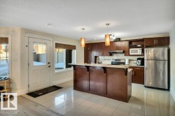 Modern kitchen featuring dark wood-finish cabinetry, stainless steel appliances, a light-toned countertop, and a tile backsplash - 