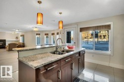 Kitchen island featuring a double basin stainless steel sink, granite countertop, and dark wood cabinetry with brushed nickel hardware - 