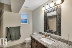 Bathroom featuring a vanity with a light-toned stone countertop, an undermount sink, and a framed mirror - 
