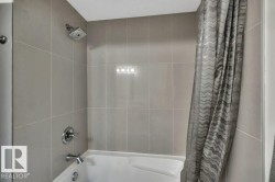 Bathtub and shower combination featuring gray tile surround, chrome fixtures, and a square shower head - 