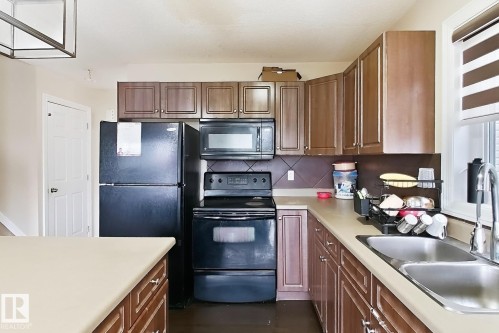 Kitchen featuring wood-finish cabinetry, solid surface countertops, a stainless steel double basin sink, and a tiled backsplash - 2829 18A Avenue Nw, Edmonton, AB 