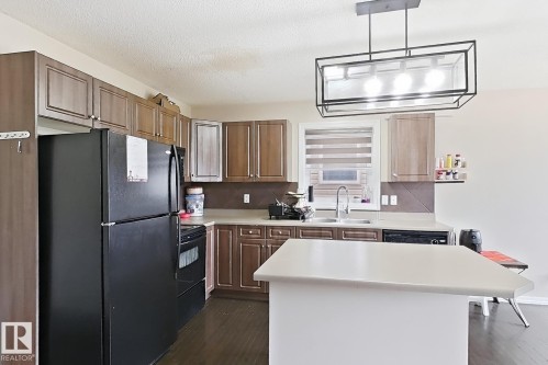 Kitchen featuring wood-finish cabinetry, a central island with a solid surface countertop, a stainless steel sink, and a contemporary linear chandelier - 2829 18A Avenue Nw, Edmonton, AB 