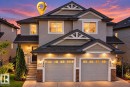 Two-story exterior with light gray siding, dark shingle roof, stone accents, two-car garage, and illuminated entrance - 2829 18A Avenue Nw, Edmonton, AB 