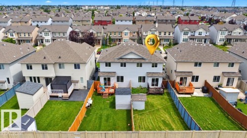 Expansive fenced backyard with a manicured lawn, a multi-level deck, two storage sheds, and a covered patio area - 2829 18A Avenue Nw, Edmonton, AB 