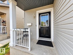 Front entry with an inviting dark paneled door featuring a window grid, light-toned horizontal siding, a substantial porch column, and a concrete porch with white railings - 