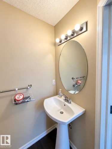 Pedestal sink with chrome fixtures, oval mirror, and a four-bulb vanity light - 2829 18A Avenue Nw, Edmonton, AB 