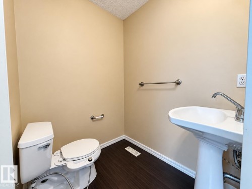 Pedestal sink with chrome faucet, toilet with bidet attachment, wood-finish flooring, and light-toned walls - 2829 18A Avenue Nw, Edmonton, AB 