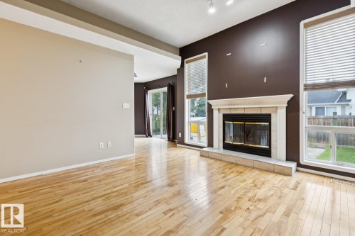 Hardwood flooring throughout, a tiled fireplace with mantel, and large windows with blinds - 1190 Potter Greens Drive Nw, Edmonton, AB 