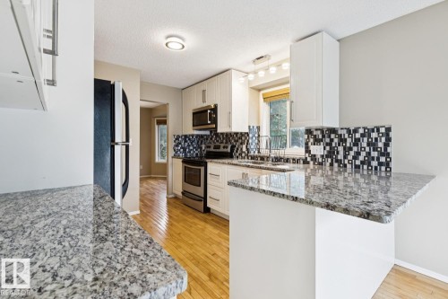 Kitchen featuring wood-finish flooring, white cabinetry, integrated stainless steel appliances, and granite countertops - 1190 Potter Greens Drive Nw, Edmonton, AB 