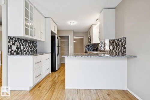 Kitchen featuring white cabinetry, a mosaic tile backsplash, wood-finish flooring, and a breakfast bar with a stone countertop - 1190 Potter Greens Drive Nw, Edmonton, AB 
