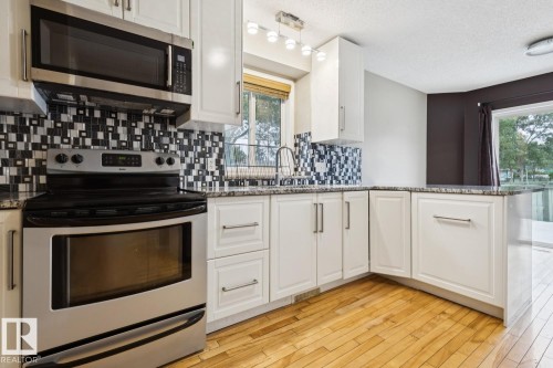 White cabinetry, stainless steel appliances, granite countertops, mosaic tile backsplash, and wood-finish flooring - 1190 Potter Greens Drive Nw, Edmonton, AB 