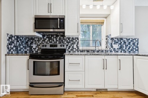 White cabinetry with brushed nickel hardware, patterned tile backsplash, stainless steel range, and stainless steel microwave - 1190 Potter Greens Drive Nw, Edmonton, AB 