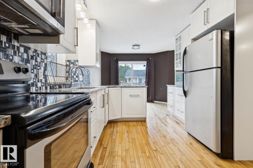 Kitchen with wood-finish flooring, white cabinetry, a mosaic tile backsplash, and stainless steel appliances - 1190 Potter Greens Drive Nw, Edmonton, AB 