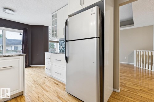 Kitchen featuring white cabinetry, light wood-finish flooring, a stainless steel refrigerator, and granite countertops - 1190 Potter Greens Drive Nw, Edmonton, AB 