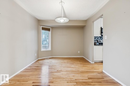 Wood-finish flooring with a bay window, a ceiling-mounted light fixture, and an open doorway to the kitchen featuring white cabinetry and a mosaic tile backsplash - 1190 Potter Greens Drive Nw, Edmonton, AB 