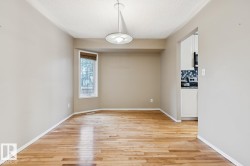 Wood-finish flooring with a bay window, a ceiling-mounted light fixture, and an open doorway to the kitchen featuring white cabinetry and a mosaic tile backsplash - 