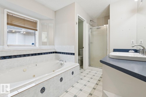 Jetted soaking tub with tiled surround, separate shower enclosure, single vanity with vessel sink, and patterned floor tile - 1190 Potter Greens Drive Nw, Edmonton, AB 