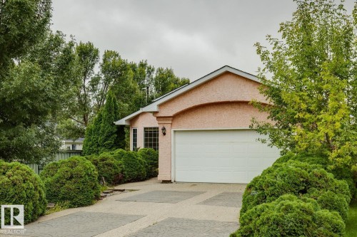 Stucco exterior with arched architectural detail, white garage door, decorative exterior lighting, multi-pane windows, and extensive mature landscaping - 1190 Potter Greens Drive Nw, Edmonton, AB 