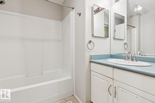 White bathtub and shower combination with a single-basin vanity featuring an oval sink and a light blue countertop - 1190 Potter Greens Drive Nw, Edmonton, AB 