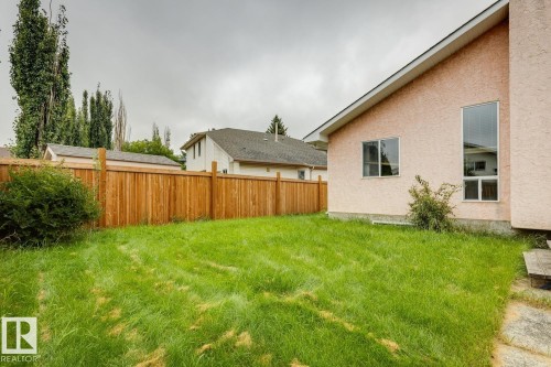 Stucco exterior with multiple windows, a long vertical window, a wooden privacy fence, and a grass lawn - 1190 Potter Greens Drive Nw, Edmonton, AB 