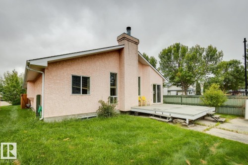 Stucco exterior with a pitched roofline, features a ground-level deck, sliding glass door access, and a prominent chimney - 1190 Potter Greens Drive Nw, Edmonton, AB 