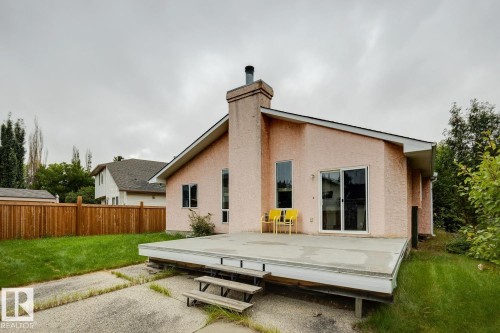 Stucco exterior with a pitched roof, featuring a built-in chimney, a sliding glass door, and an elevated patio deck with steps - 1190 Potter Greens Drive Nw, Edmonton, AB 