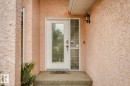 Stucco exterior with a glass-paneled entry door, sidelight, and wall-mounted exterior light fixture - 1190 Potter Greens Drive Nw, Edmonton, AB 