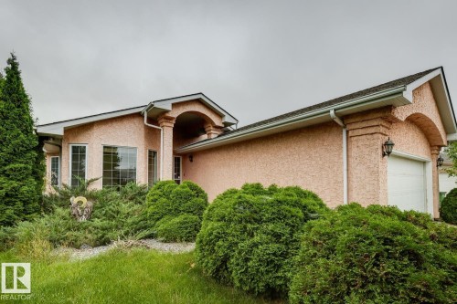Stucco exterior with a peaked roofline, arched entry, multiple windows, and an attached garage - 1190 Potter Greens Drive Nw, Edmonton, AB 