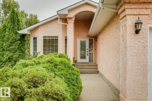 Stucco exterior with arched entryway, decorative outdoor lighting, multi-pane windows, and concrete front steps - 1190 Potter Greens Drive Nw, Edmonton, AB 