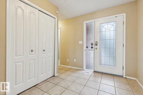 Entryway featuring tile flooring, a decorative glass entry door, an opaque glass sidelight, and bi-fold closet doors - 1190 Potter Greens Drive Nw, Edmonton, AB 
