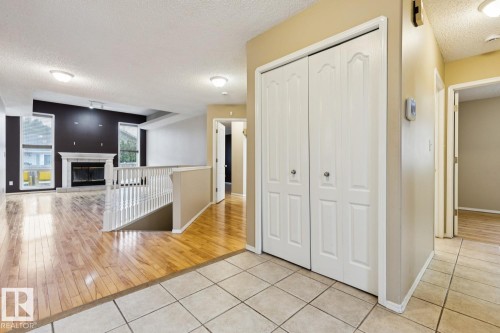 Ceramic tile flooring, wood-finish flooring, white bi-fold closet doors, white staircase railing, and a fireplace with a white mantel - 1190 Potter Greens Drive Nw, Edmonton, AB 