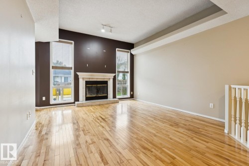 Hardwood flooring, fireplace with stone surround and hearth, tall windows, track lighting, and a white balustrade - 1190 Potter Greens Drive Nw, Edmonton, AB 