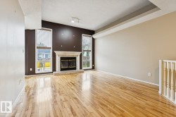 Hardwood flooring, fireplace with stone surround and hearth, tall windows, track lighting, and a white balustrade - 