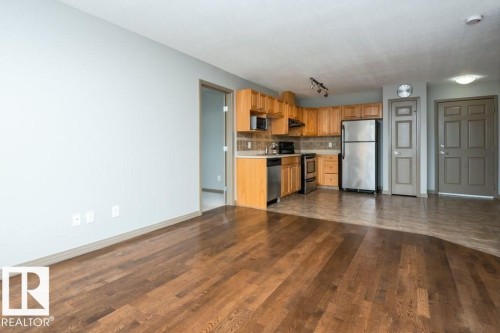 Hardwood flooring, full kitchen with wood-finish cabinetry, stainless steel appliances, tile backsplash, and track lighting - 401 5005 165 Avenue Nw, Edmonton, AB 