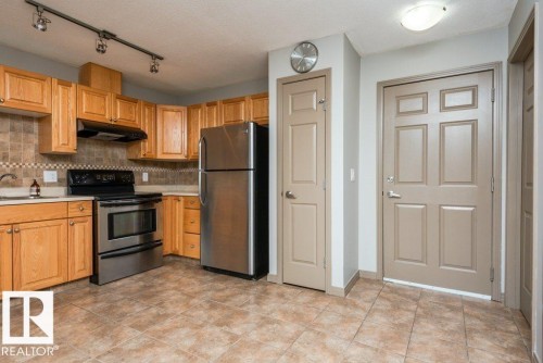 Kitchen featuring wood cabinetry, stainless steel appliances, tiled backsplash, and tile flooring - 401 5005 165 Avenue Nw, Edmonton, AB 