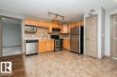 Kitchen featuring wood cabinetry, stainless steel appliances, tile flooring, and a tile backsplash - 401 5005 165 Avenue Nw, Edmonton, AB 