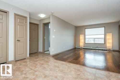 Expansive room featuring wood-finish flooring, a large window with roller shade, and neutral wall tones - 401 5005 165 Avenue Nw, Edmonton, AB 