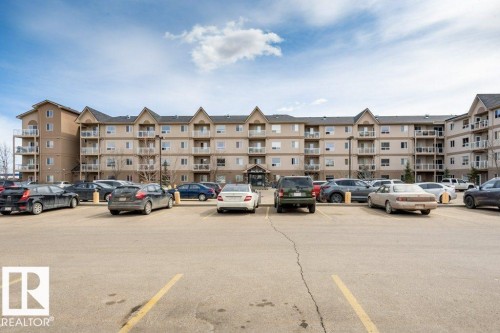 Multi-story building with a neutral-toned exterior, multiple private balconies, and an asphalt parking lot - 401 5005 165 Avenue Nw, Edmonton, AB 