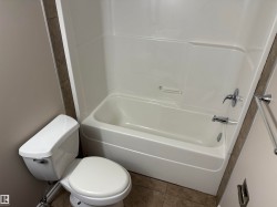 White toilet, white bathtub with integrated shower, chrome fixtures, and neutral-toned wall tiles - 