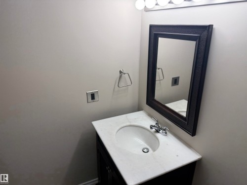 Vanity with a white countertop and integrated sink, chrome faucet, framed wall mirror, and overhead vanity lighting - #205 10335 117 St Nw, Edmonton, AB 