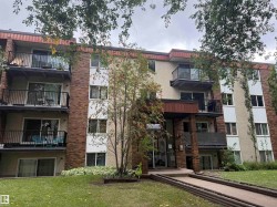 Multi-story building featuring stucco and brick exterior, individual balconies with black railings, and a prominent covered entryway - 