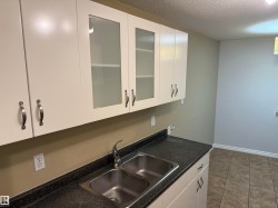 White cabinetry with brushed nickel hardware, a dual basin stainless steel sink, black speckled countertops, and a tiled floor - 