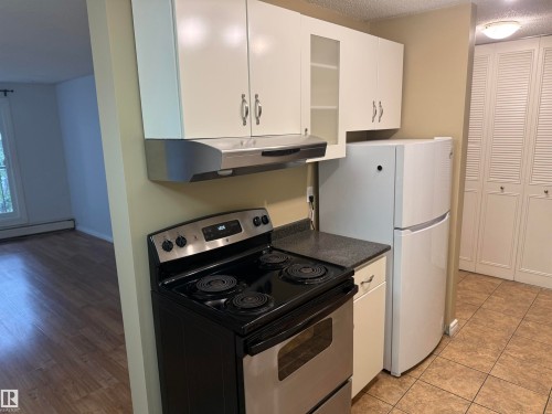Stainless steel range, white upper cabinetry, built-in range hood, dark countertop, and tiled flooring - #205 10335 117 St Nw, Edmonton, AB 