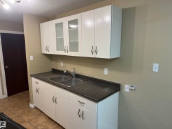 White cabinetry with brushed nickel hardware, dual-basin stainless steel sink, dark countertop, and tiled flooring - 
