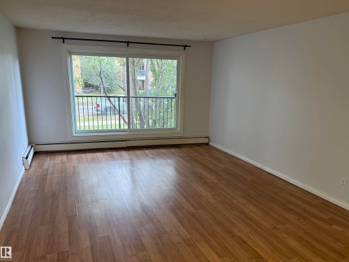 Wood-finish flooring with white baseboards, large sliding glass door, and a balcony with metal railings - #205 10335 117 St Nw, Edmonton, AB 