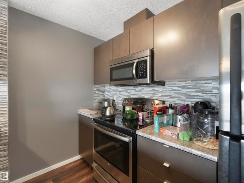 Stainless steel appliances, built-in microwave, wood-finish flooring, stone-finish countertops, and mosaic tile backsplash - #414 340 Windermere Rd Nw, Edmonton, AB 