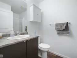 Vanity with an integrated sink and chrome faucet, wood-finish flooring, white wall-mounted cabinet, and a shower with a sliding glass door - 