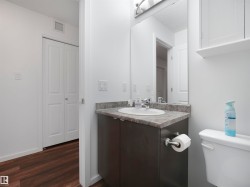 Bathroom featuring a vanity with a counter and integrated sink, a wall-mounted mirror, overhead lighting, and wood-finish flooring - 
