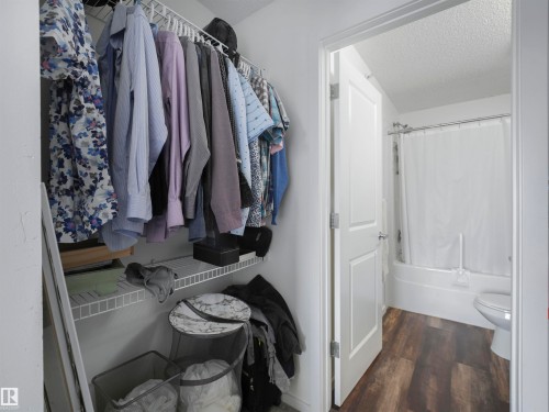 Built-in wired shelving system, wood-finish flooring, white paneled door, and a full bathtub with shower - #414 340 Windermere Rd Nw, Edmonton, AB 